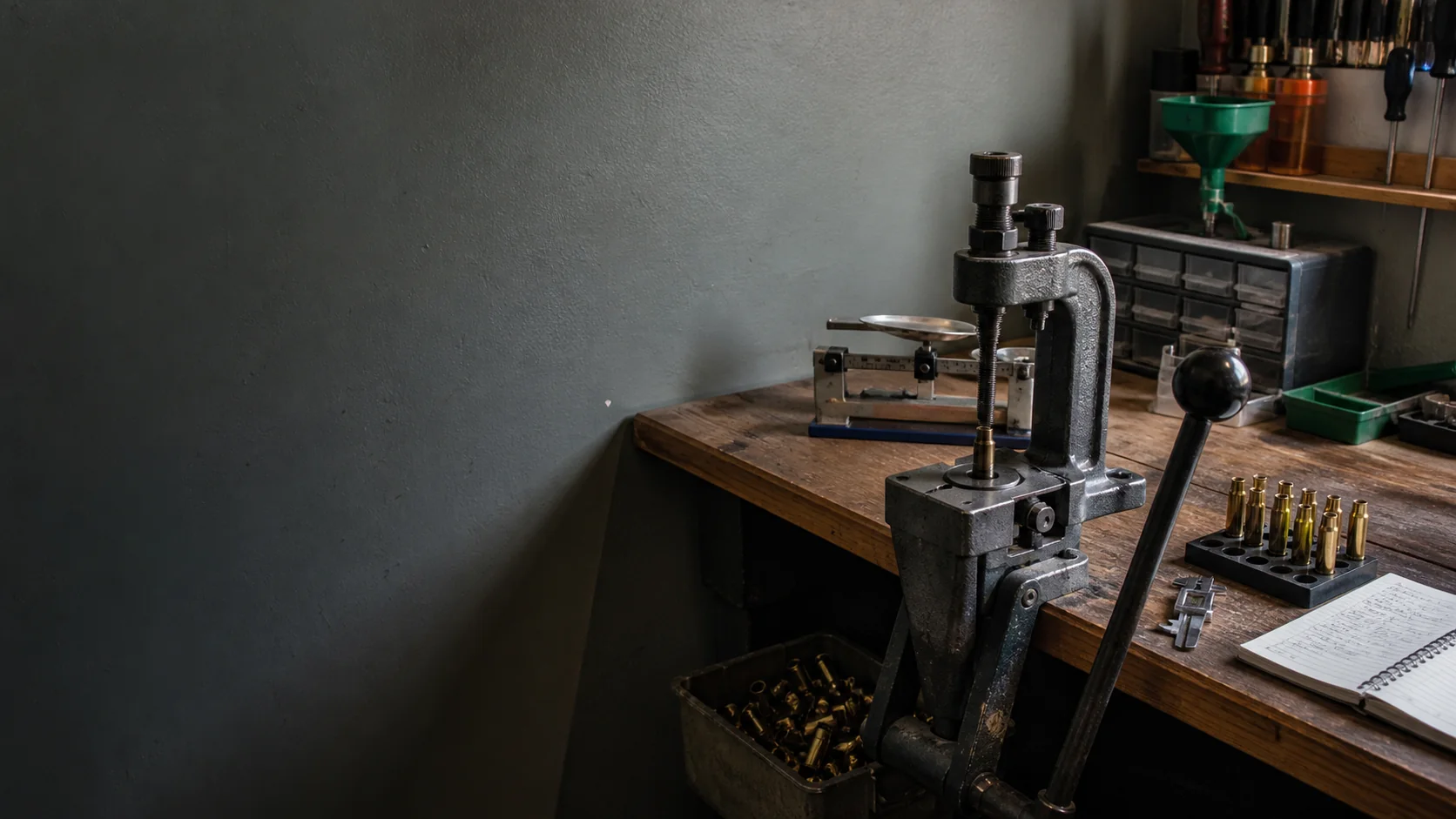 A practical reloading bench with press, scale, cases, calipers, and notebook